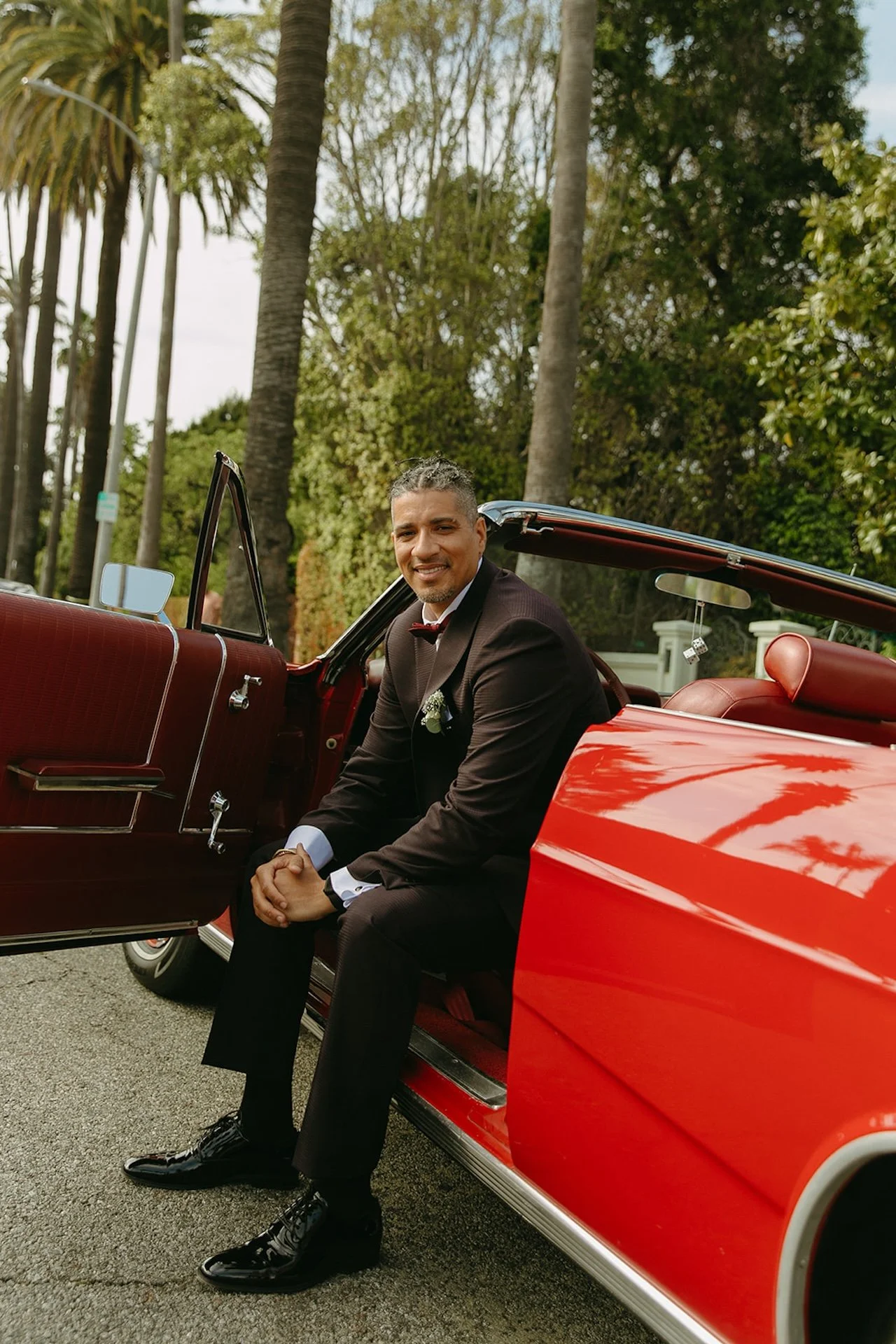 A groom portrait of him leaning out of a red convertable in the driver seat after his Beverly Hills Courthouse Elopement