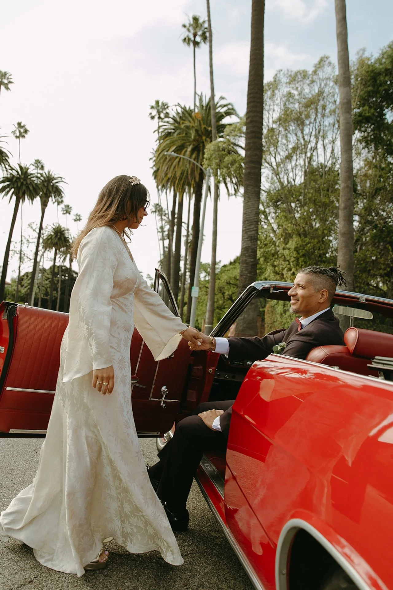 A candid shot of the bride and groom holding hands in the front seat of a red convertable during their Beverly Hills Courthouse Elopement
