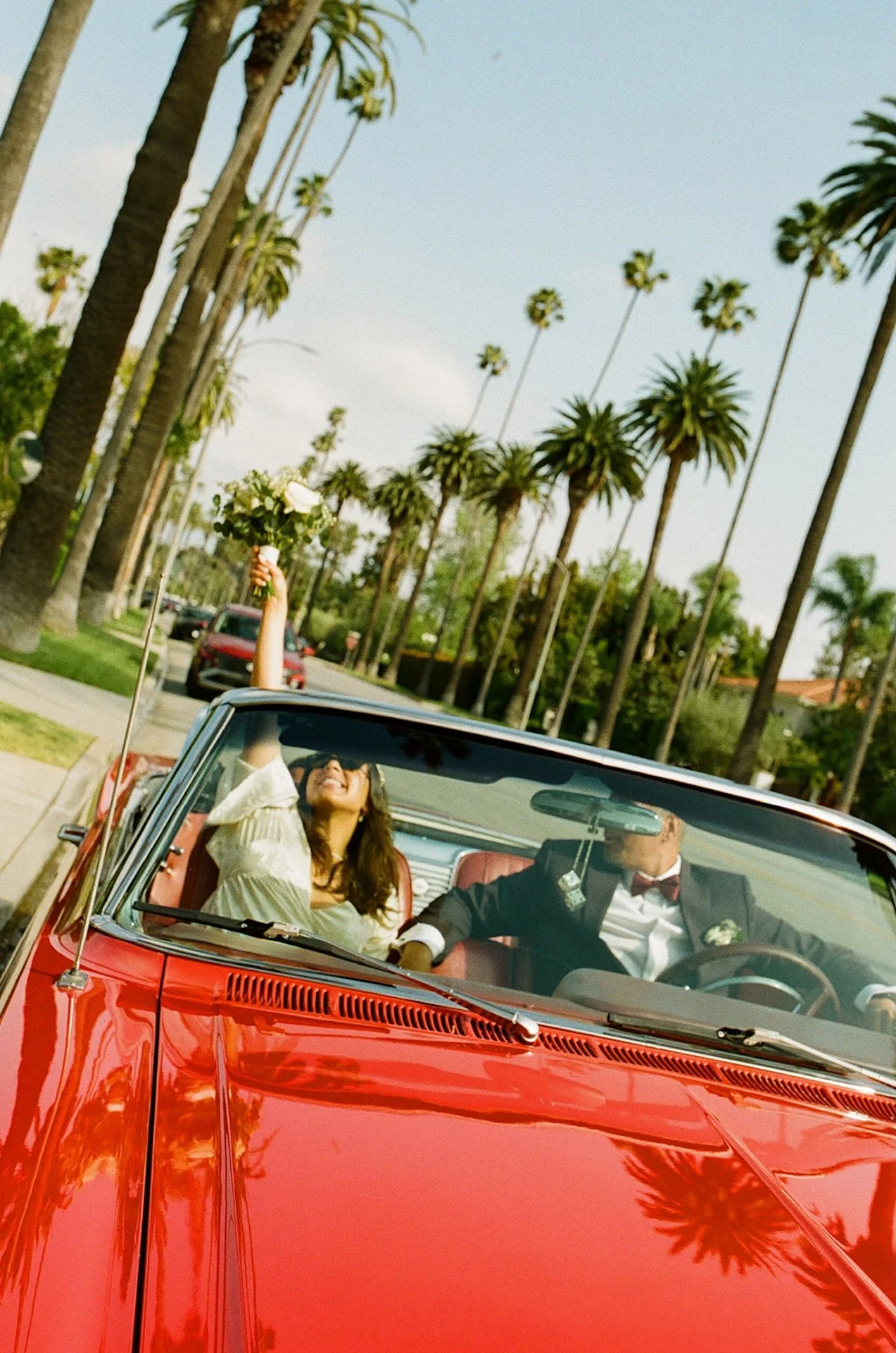 Film photo of the bride and groom sitting in a red convertable after their Beverly Hills Courthouse Elopement with the bride holding her bouquet out the sunroof