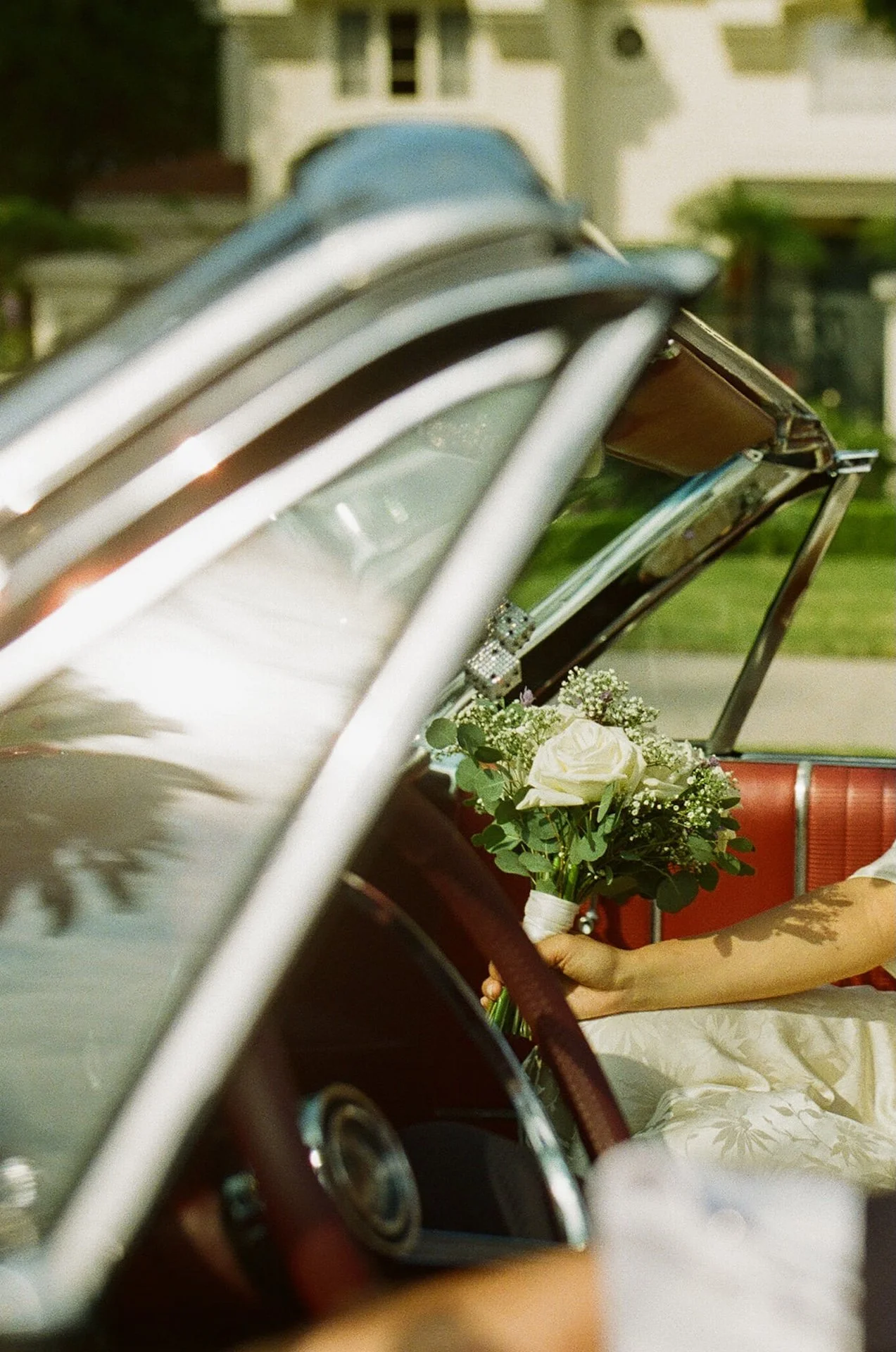 A editorial film photo of the bride holding her bouquet in the front seat of a red convertable after their Beverly Hills Courthouse Elopement