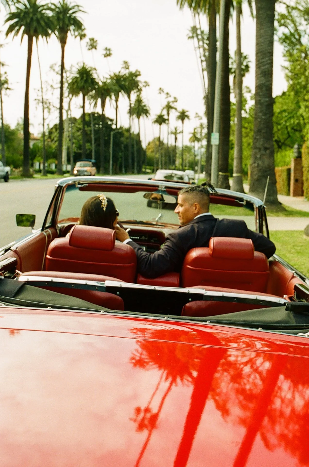 Newlyweds sitting in the front seat of a red convertable and chatting, smiling, and kissing after their Beverly Hills Courthouse Elopement
