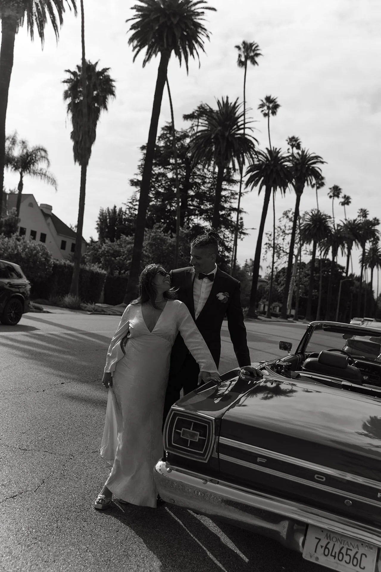 A black and white photo of the newlyweds leaning against a convertable during their bride and groom portraits in Beverly Hills