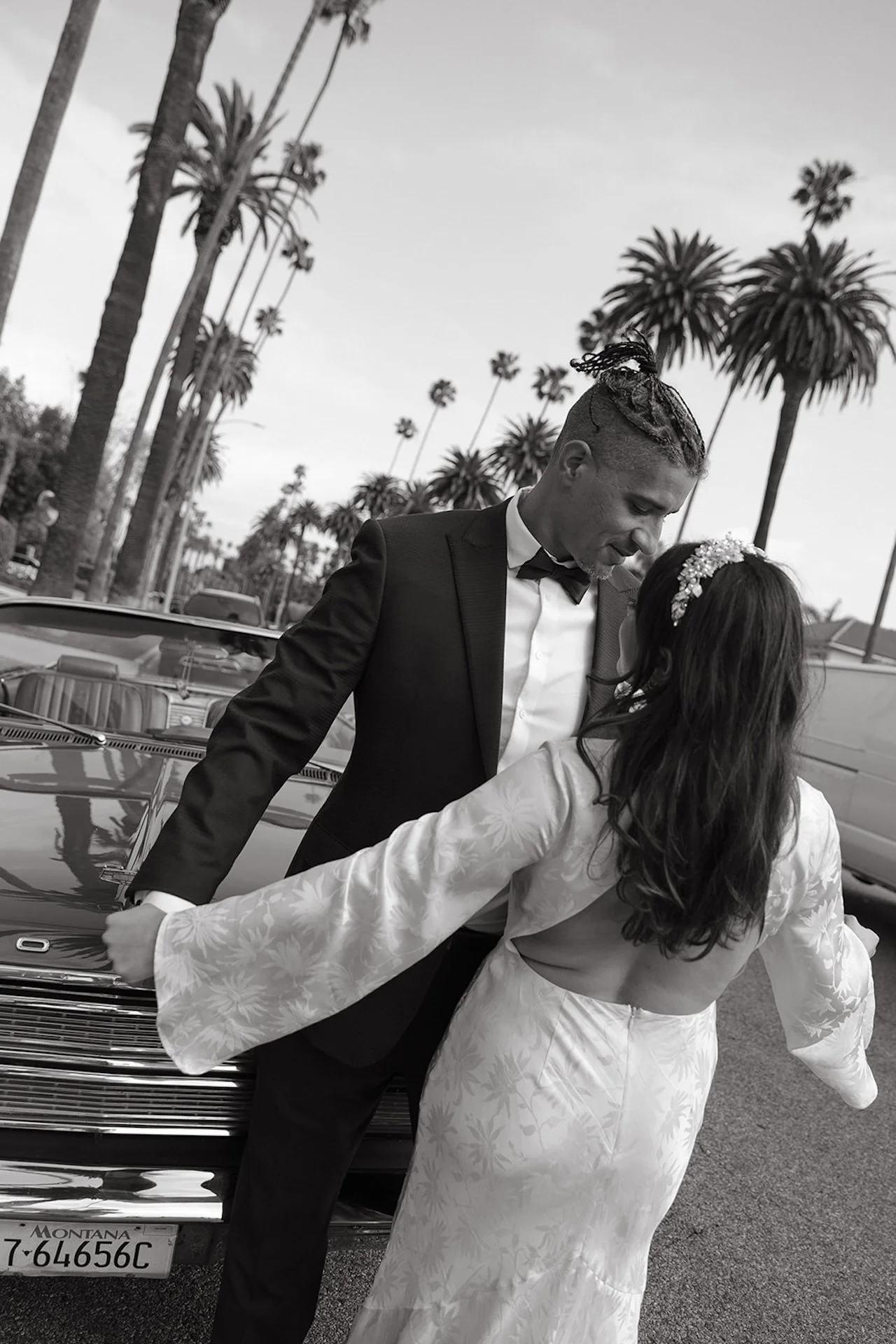 Bride and groom dancing in front of a convertable on a palm tree lined street