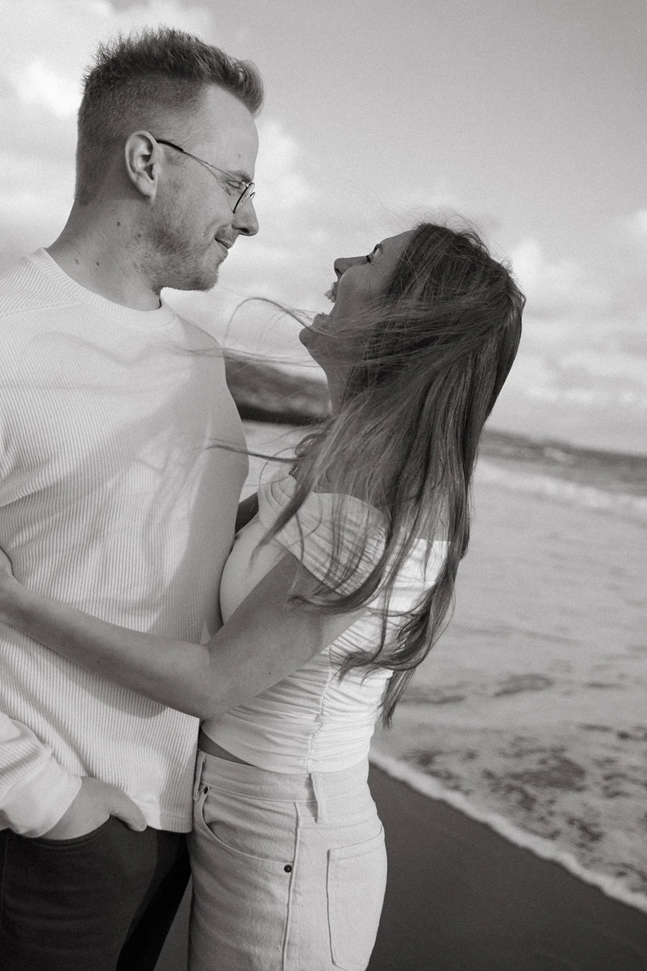 Black and white photo of a couple hugging and laughing while smiling during their engagement shoot