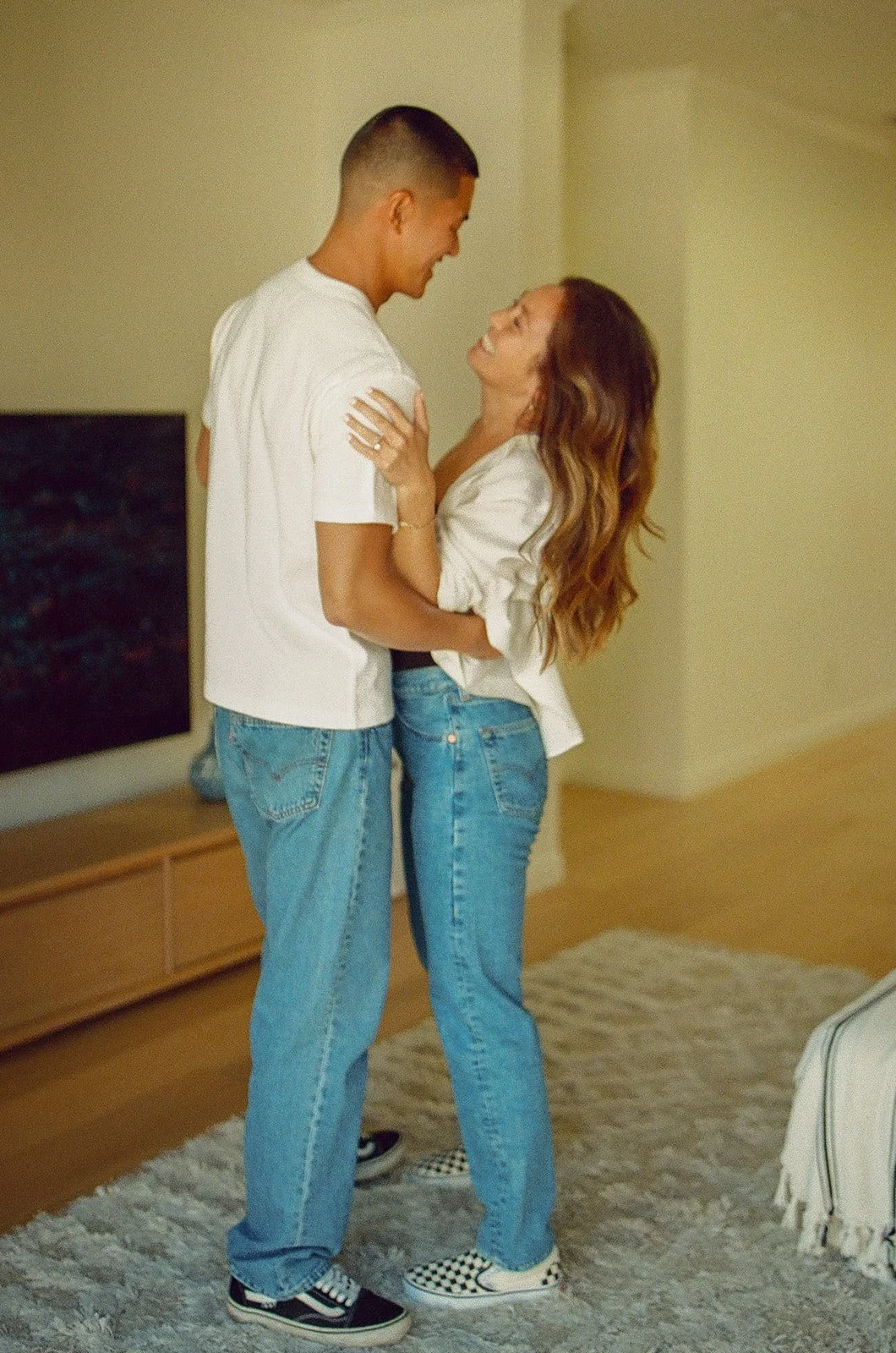 A couple standing together indoors laughing and leaning into each other during a relaxed lifestyle session.