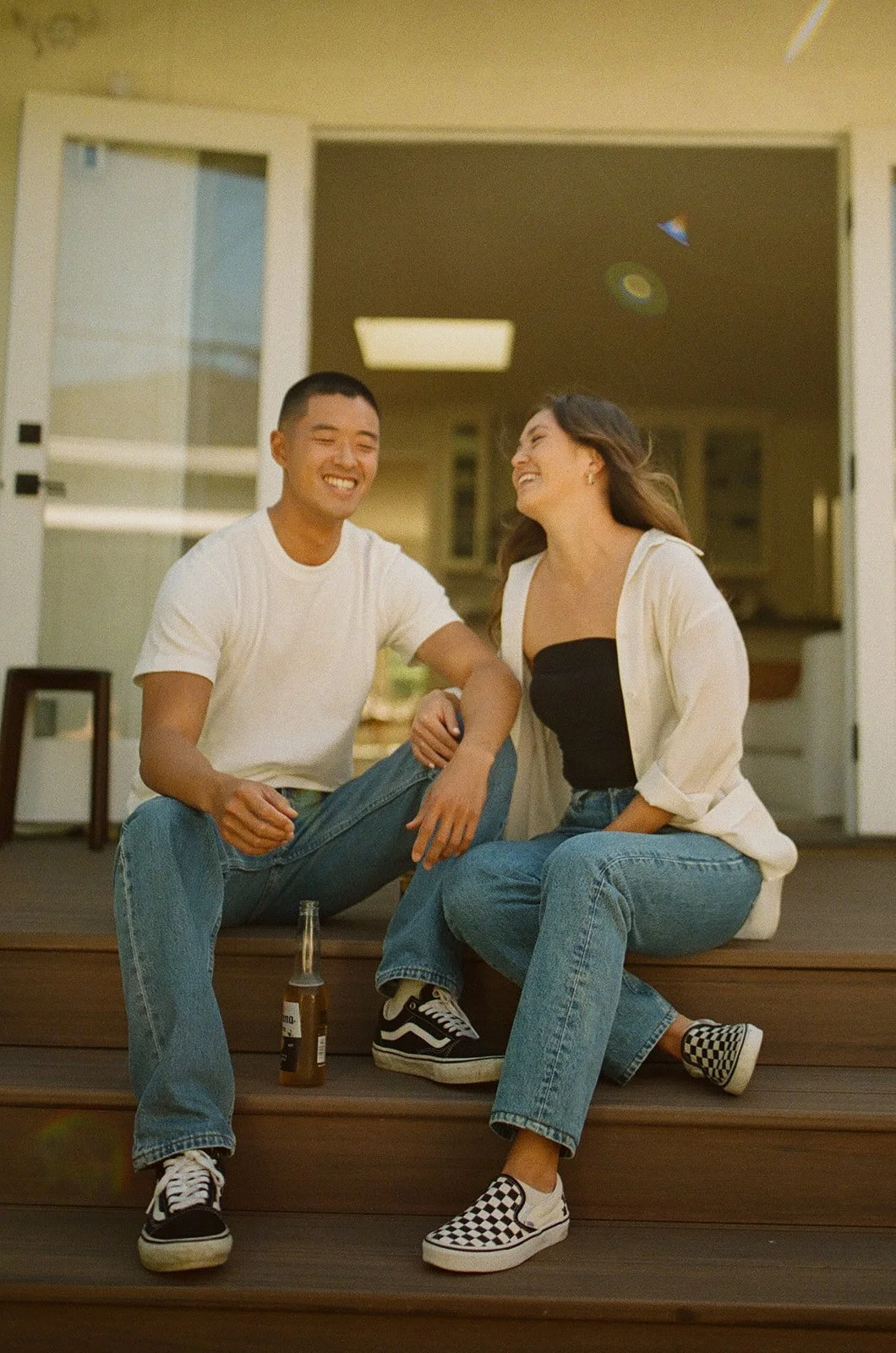 A couple sitting on wooden steps laughing together in casual outfits with warm afternoon light.