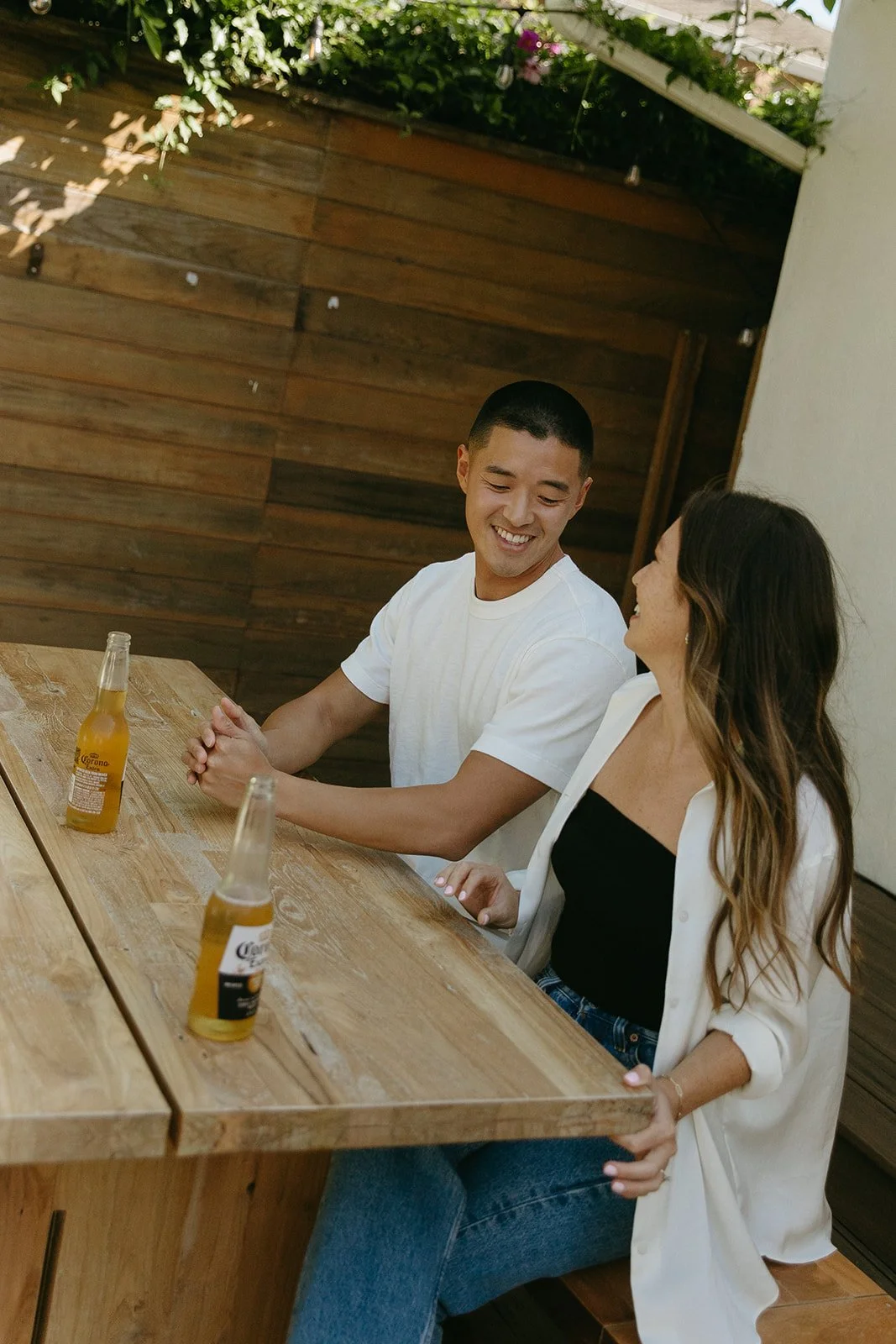 A couple sitting at an outdoor table laughing together during a casual lifestyle engagement session.