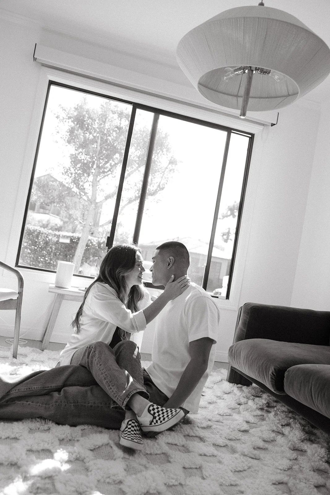 A couple sitting close together at a small round table by a window, sharing a quiet laugh.