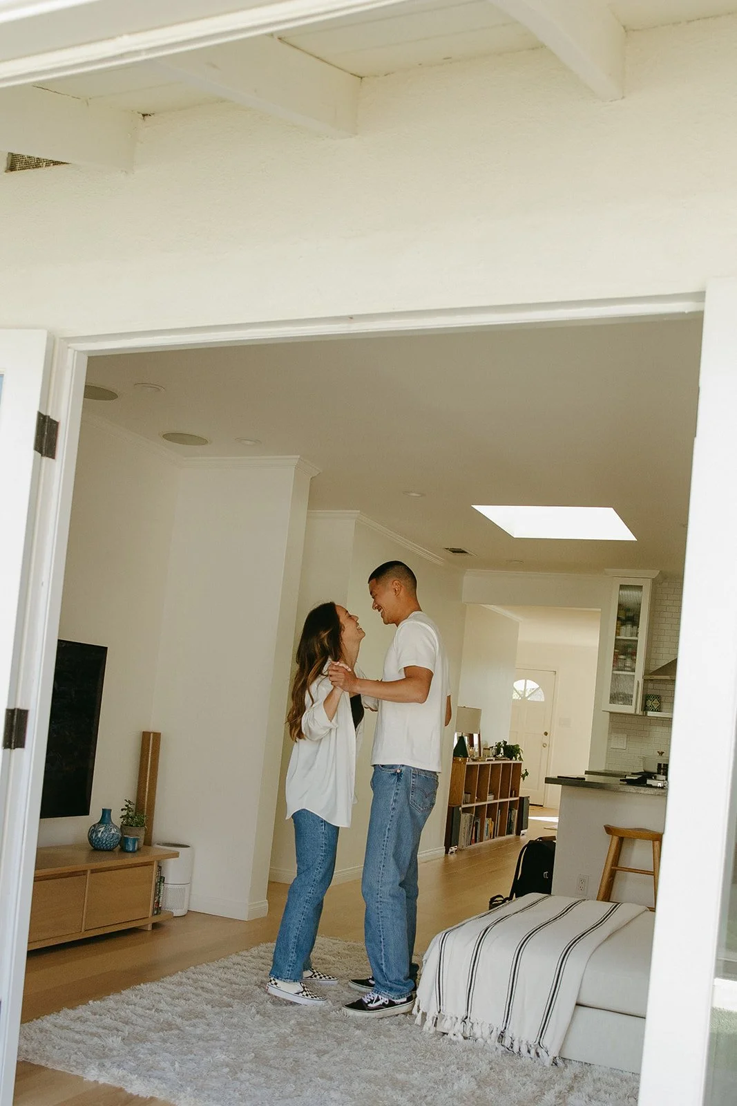 A couple standing close together in their living room, smiling and holding each other in a relaxed at-home moment.