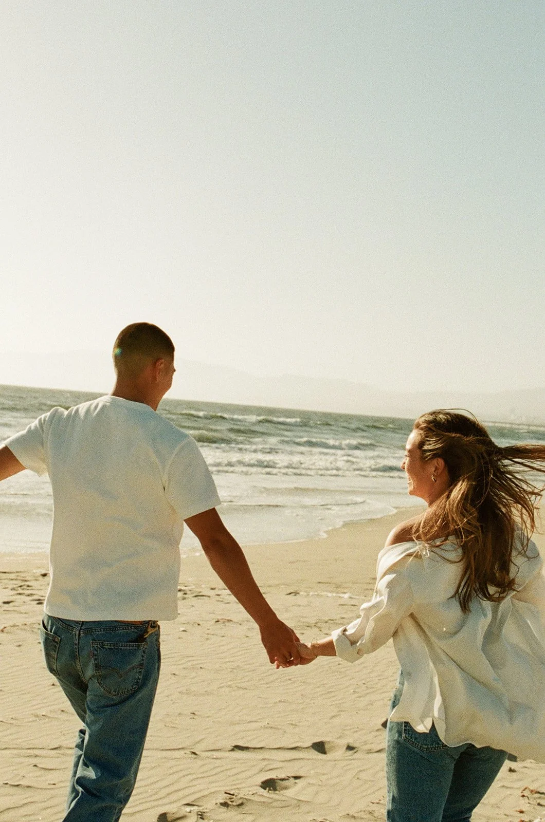 A carefree beach interaction captured at Venice Beach Photoshoot Locations with soft sand, rolling waves, and warm evening light.