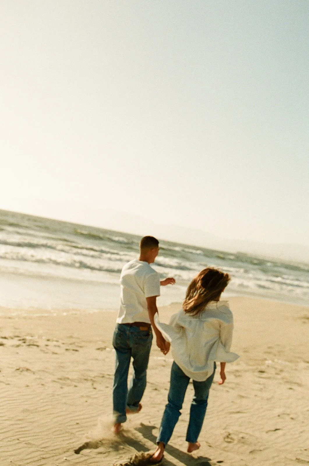A golden hour beach portrait taken at Venice Beach Photoshoot Locations with ocean waves, backlit light, and wind moving through her hair.