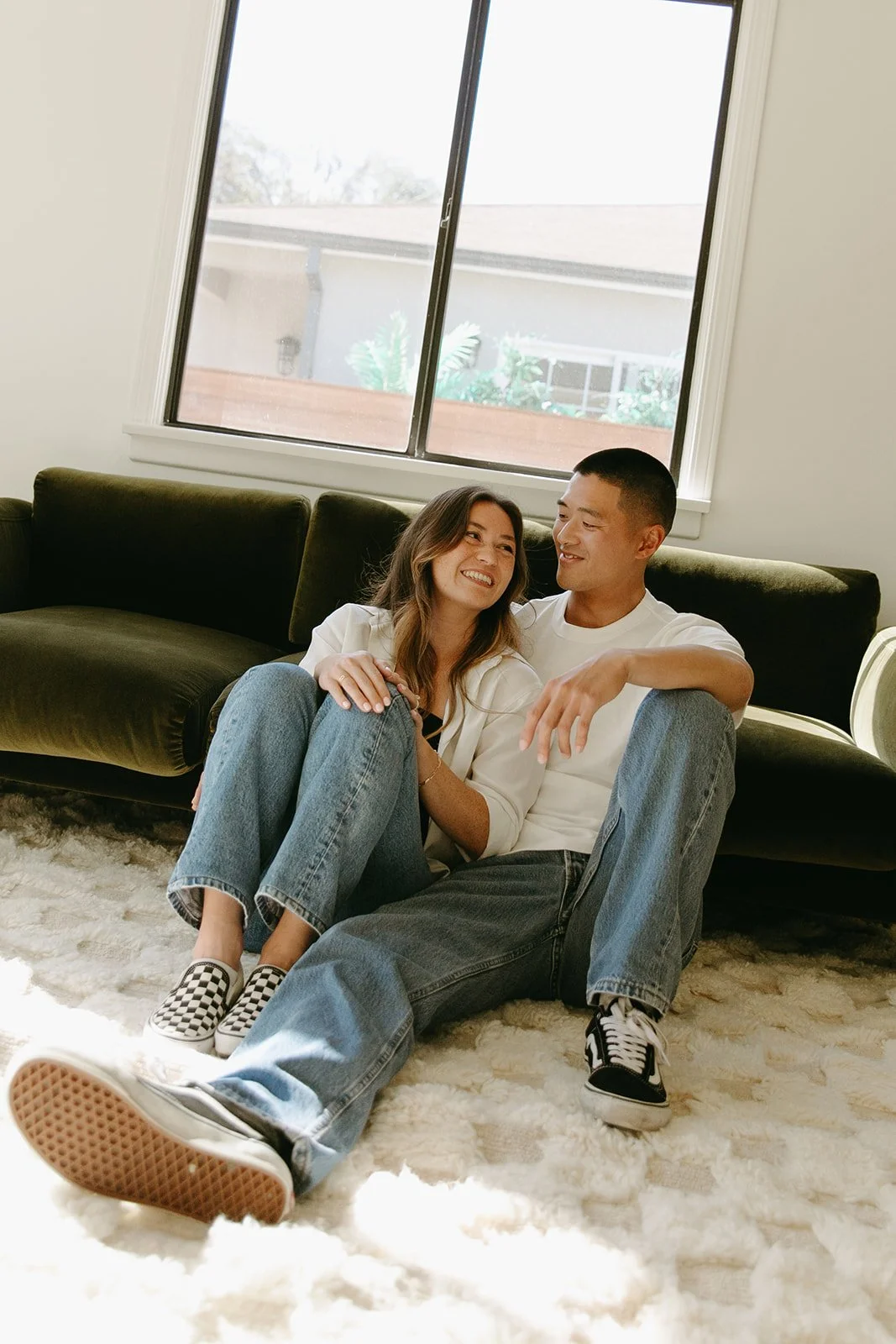 A cozy indoor lifestyle portrait captured at Venice Beach Photoshoot Locations with a couple sitting on the floor, leaning into each other with soft window light.