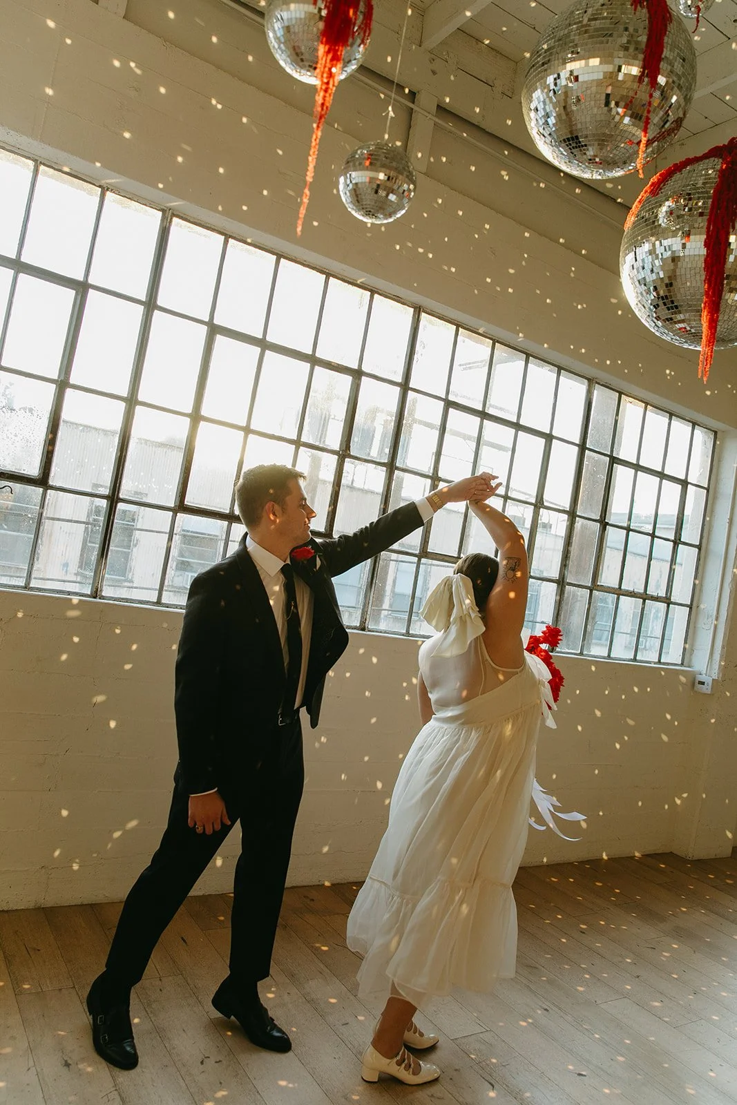 A couple dancing together under disco balls with sunlight streaming through the windows at The Revery LA, creating a fun and intimate wedding moment.