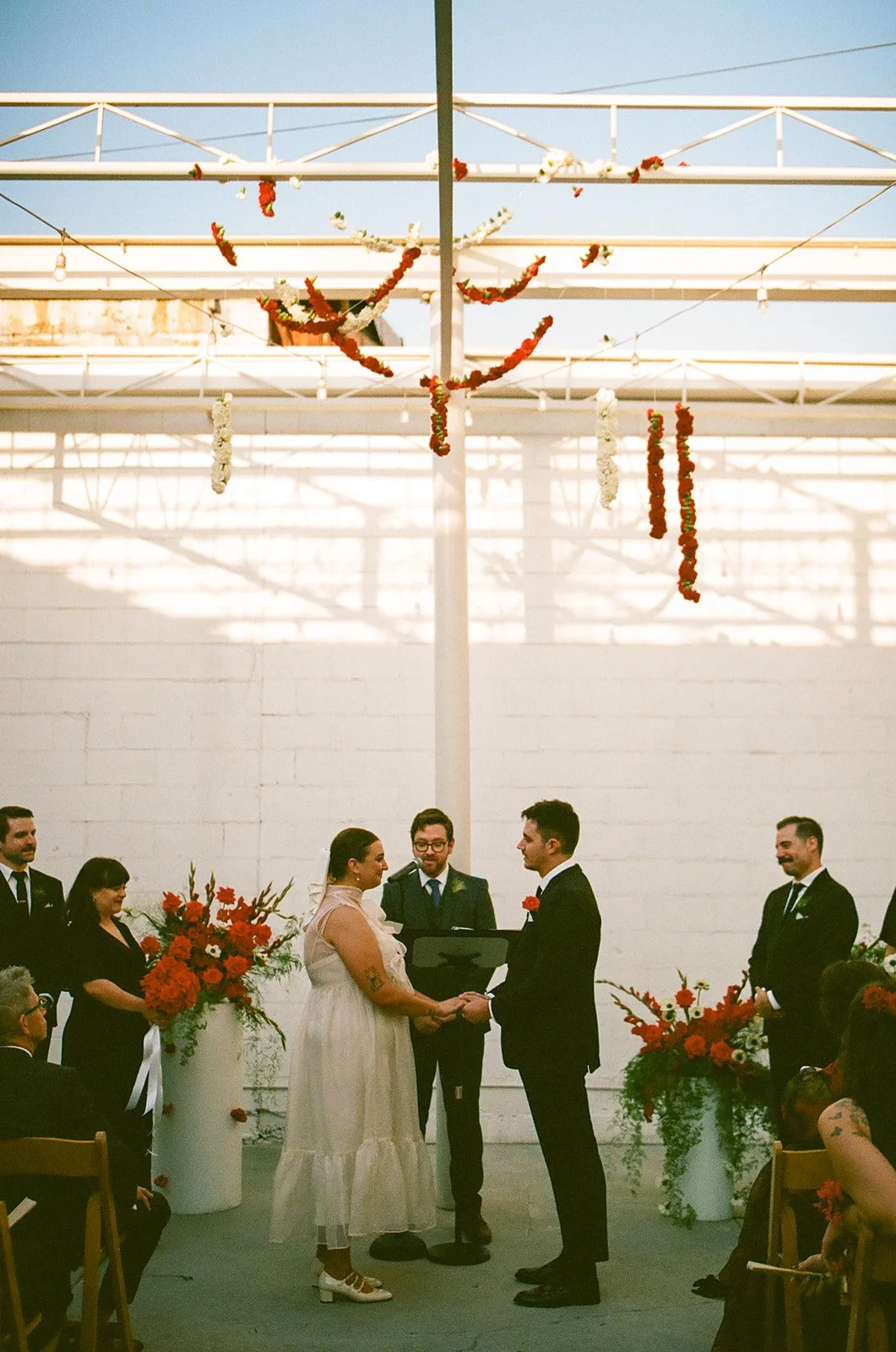 A wide view of the wedding ceremony at The Revery LA with guests seated and floral installations hanging above the couple as they exchange vows.
