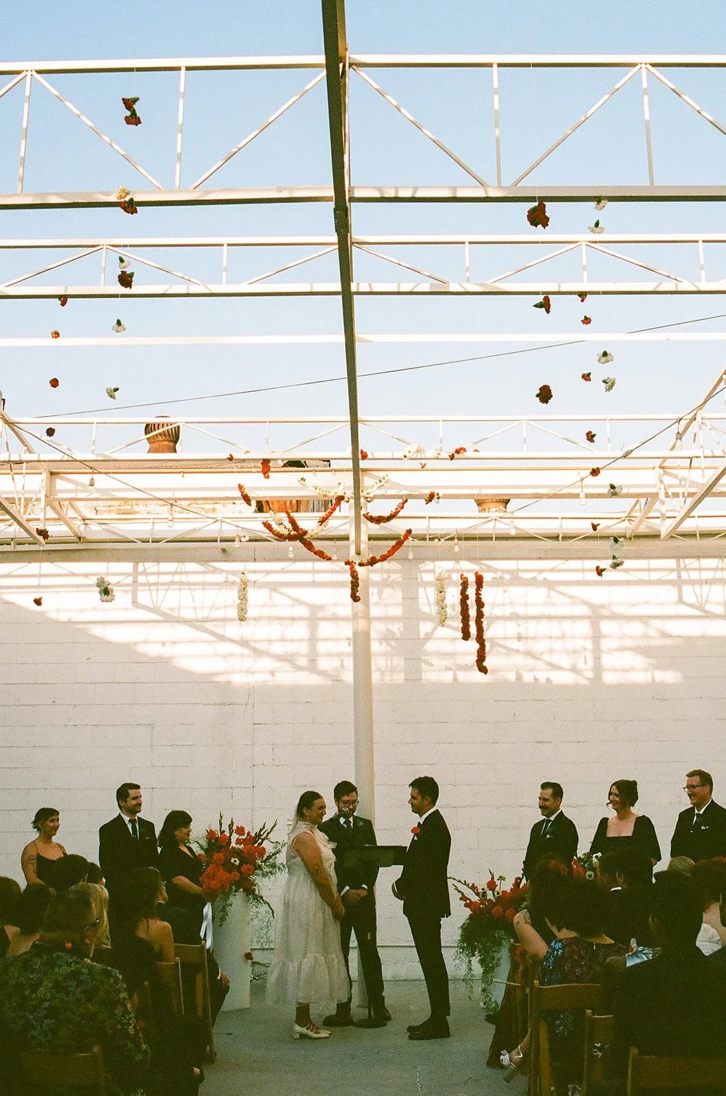 A wide view of the wedding ceremony at The Revery LA with guests seated and floral installations hanging above the couple as they exchange vows.