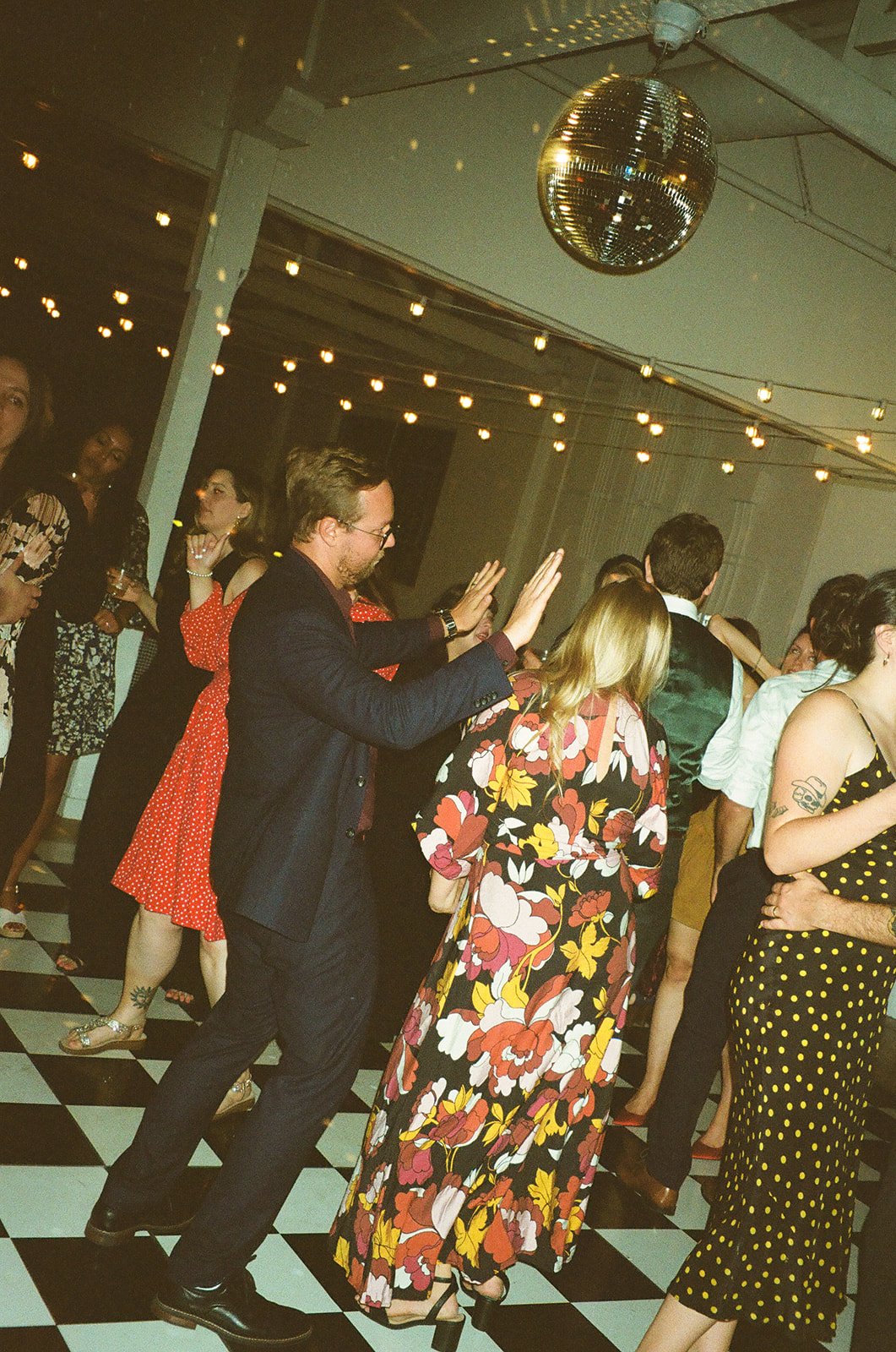 Guests dancing together under disco balls on the checkered floor at The Revery LA during the evening celebration.