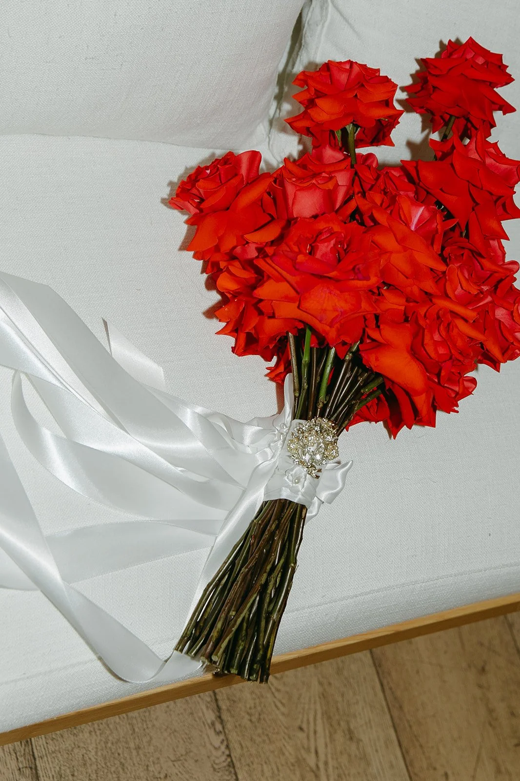 A bright red rose bouquet wrapped with white ribbon resting on a light couch inside The Revery LA before the ceremony.