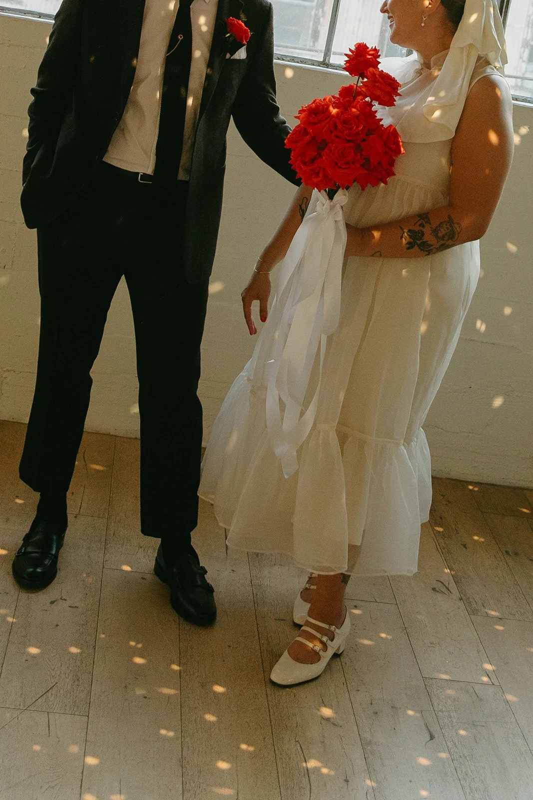 A close view of the couple holding a bright red bouquet near the windows at The Revery LA, with warm light and reflections around them.