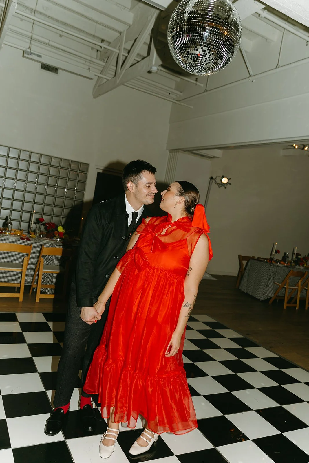 The couple holding hands and smiling at each other beneath a disco ball at The Revery LA during the reception.