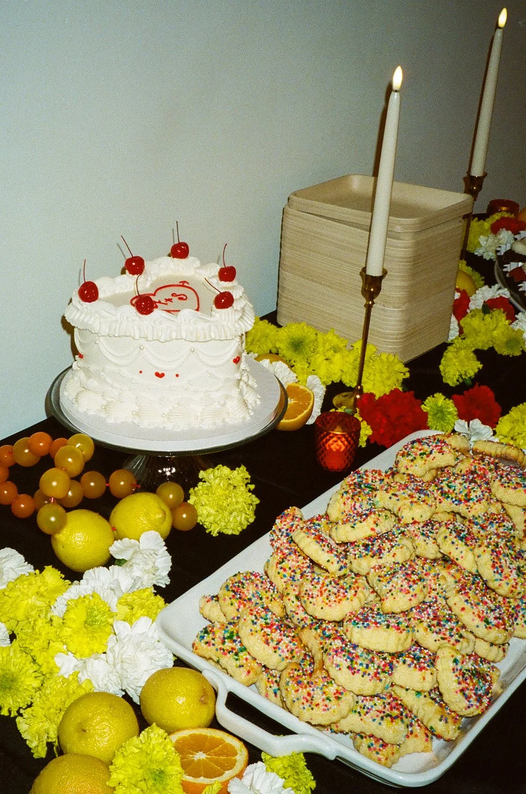 A dessert table at The Revery LA with a vintage-style cake, colorful cookies, citrus, candles, and floral details.