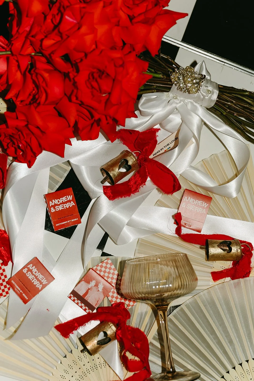 Close-up of a red rose bouquet with white ribbon and vintage bells styled on a table at The Revery LA.
