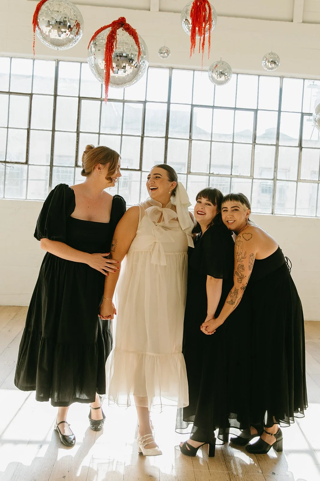 Bridesmaids standing with the bride inside The Revery LA, laughing together beneath hanging disco balls and large industrial windows.