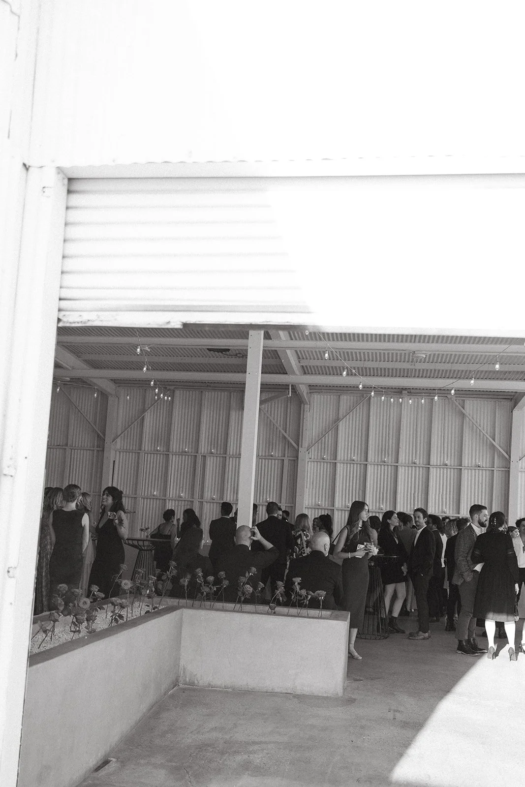Guests mingling and chatting during cocktail hour inside The Revery LA, captured in a candid black and white moment.