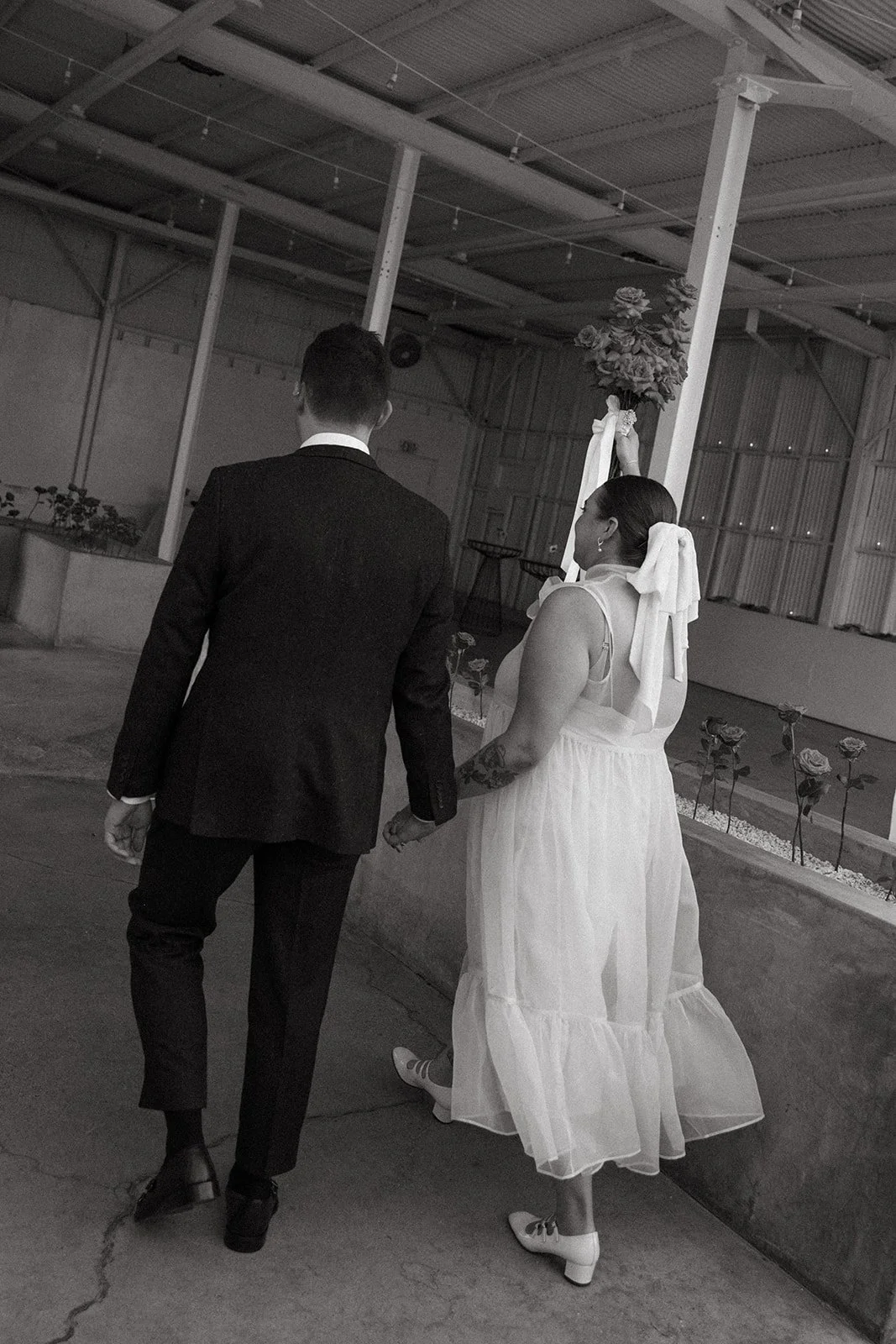 A black and white photo of the bride and groom holding hands and walking into their wedding reception at The Revery LA
