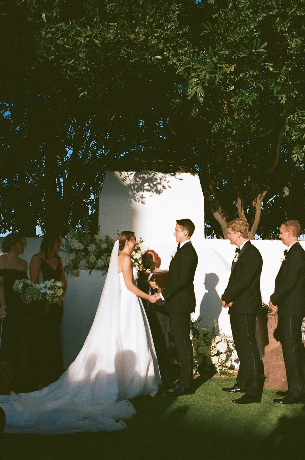 Ceremony moment at a classic San Clemente Wedding Venue with the couple exchanging vows beneath trees and warm string lighting.