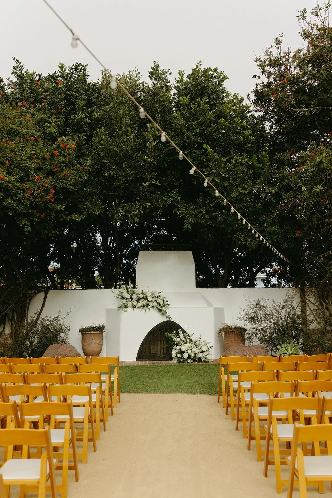 Outdoor ceremony space with wooden chairs, greenery, and a white fireplace backdrop at a coastal Southern California venue.