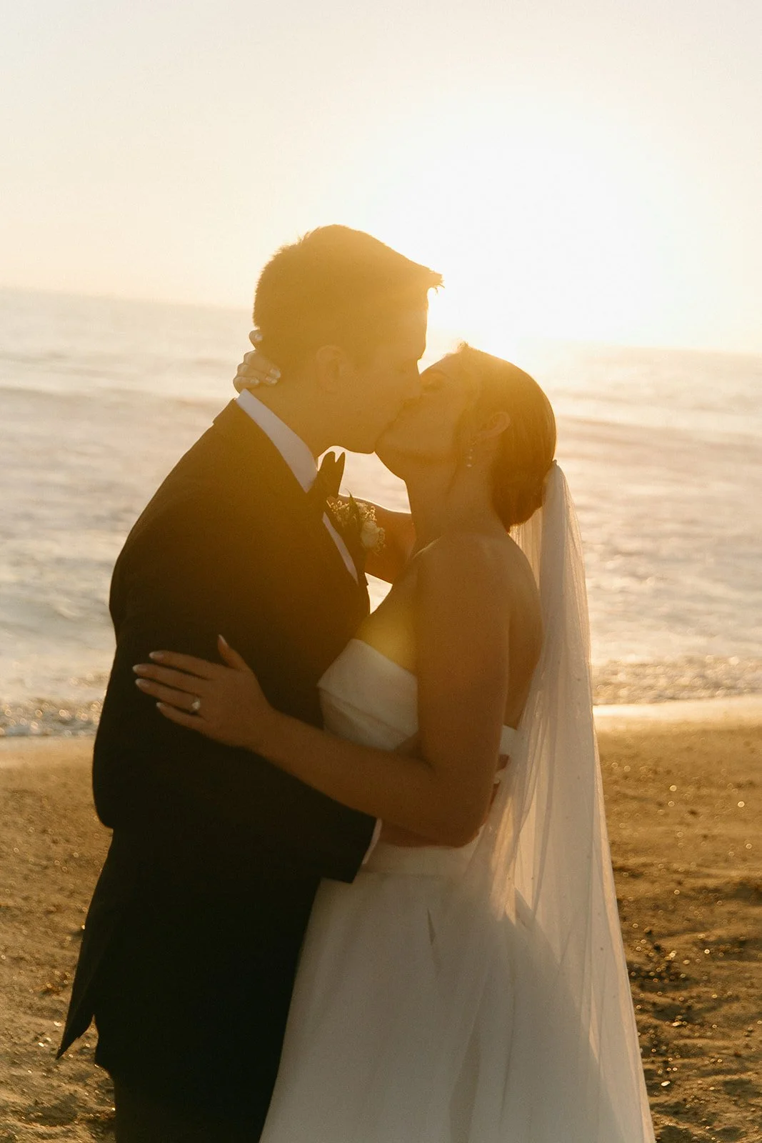 The bride and groom sharing a kiss on the beach during sunset with the golden hour colors all around them.