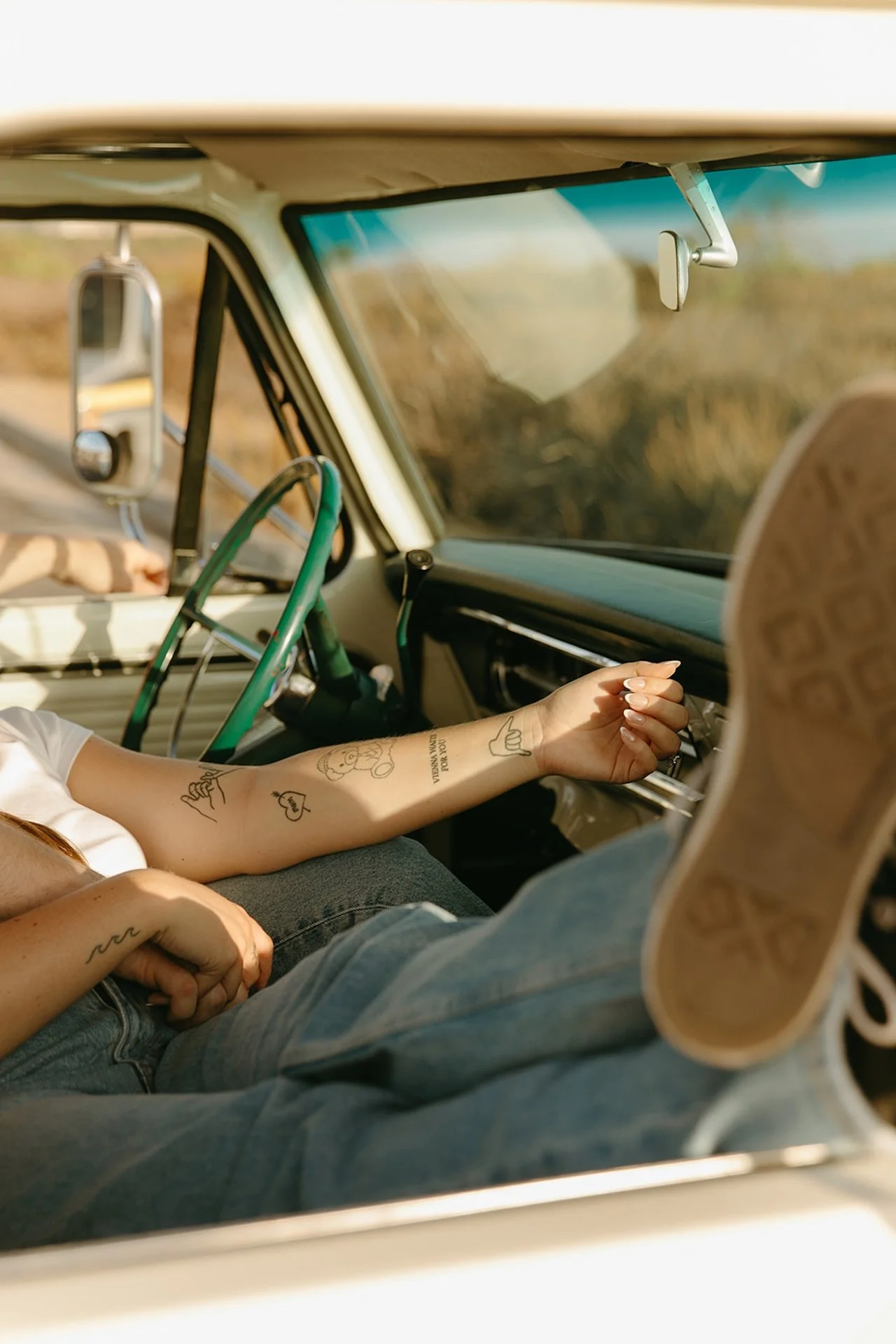 A close-up of a woman’s arm with minimalist tattoos resting near the truck dashboard, with soft sunlight highlighting the interior details.