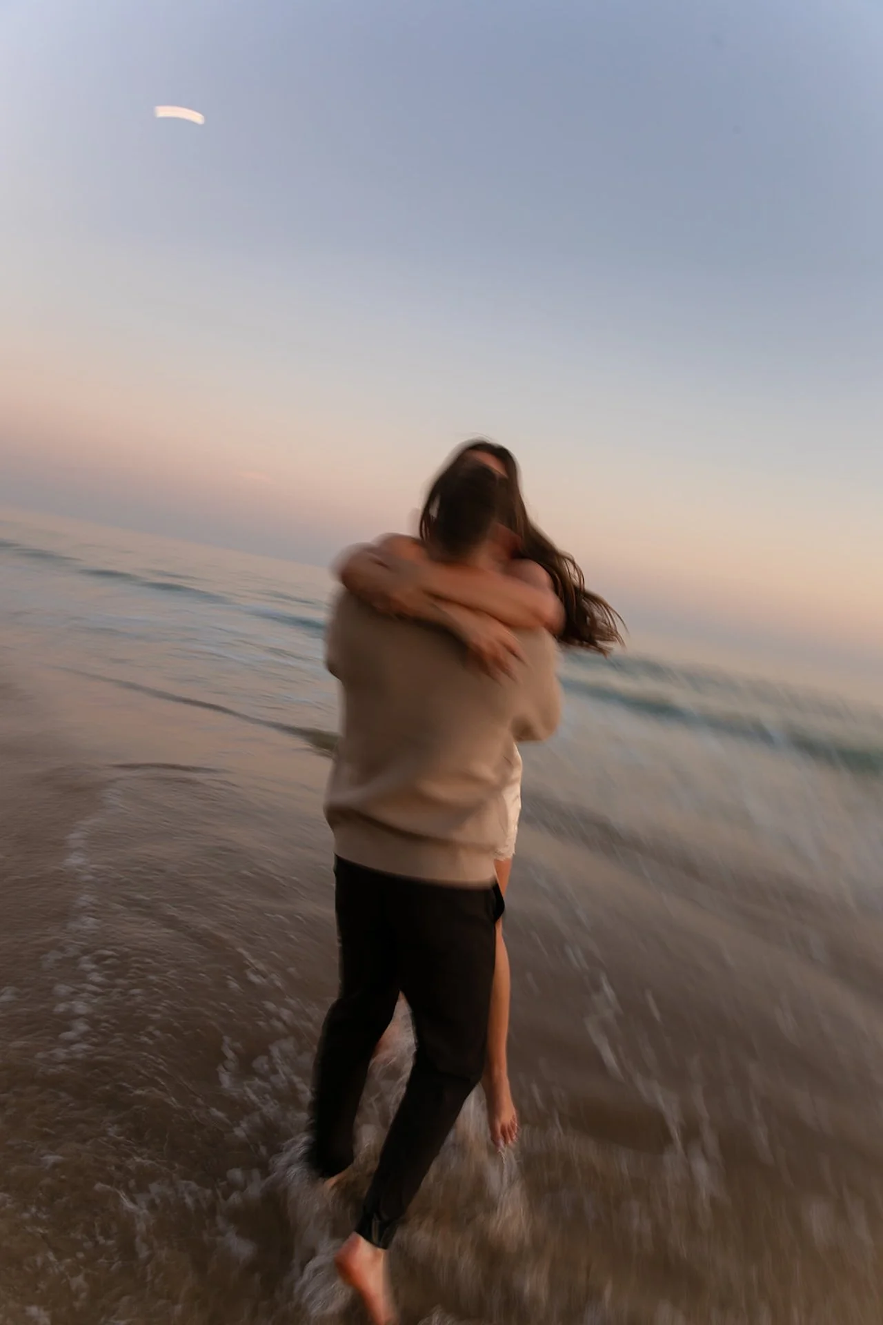 A romantic motion-blur image of a couple hugging in the ocean surf at sunset, with soft waves and a dreamy coastal horizon.