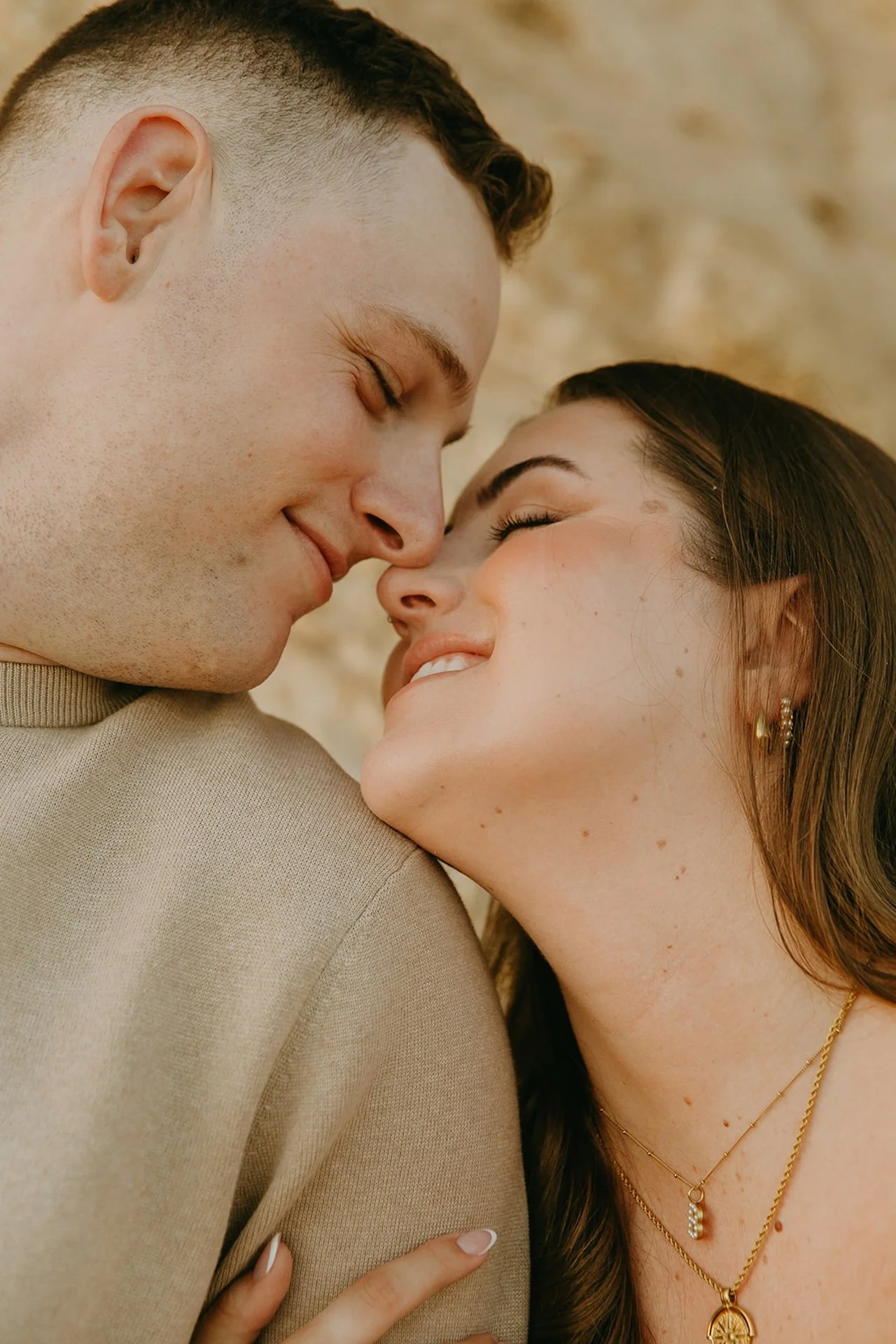 Beach Engagement Photo Ideas of a close-up of a couple smiling and touching noses, with soft golden light and natural coastal textures behind them.
