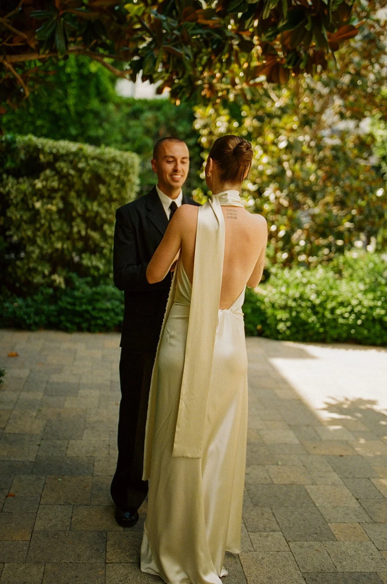 The bride and groom facing each other during a private moment in a garden courtyard, with greenery and soft natural light creating a romantic, intimate setting.