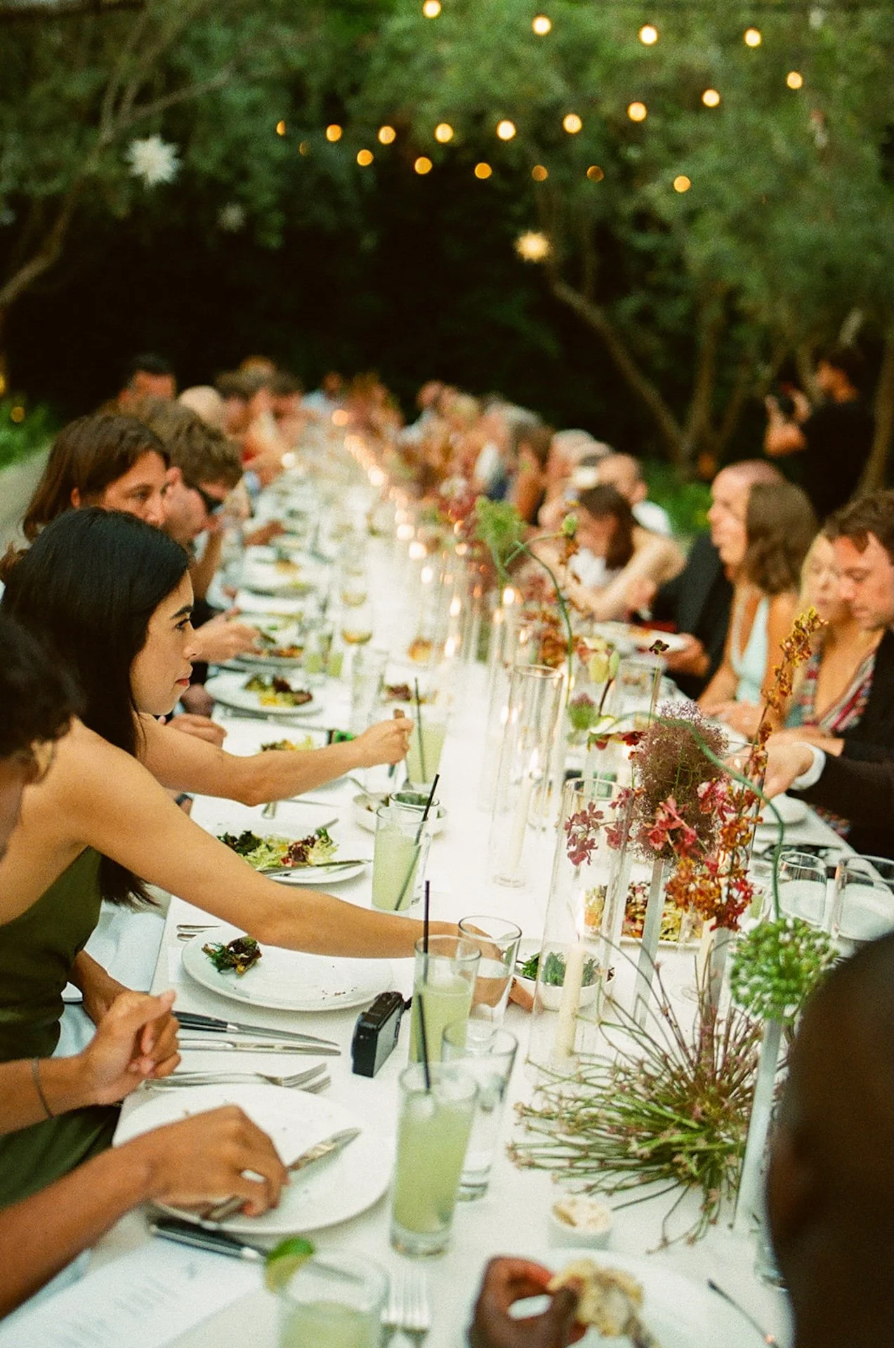 A long banquet table filled with guests dining outdoors under string lights, creating a cozy atmosphere for Intimate Wedding Ideas and small wedding receptions.