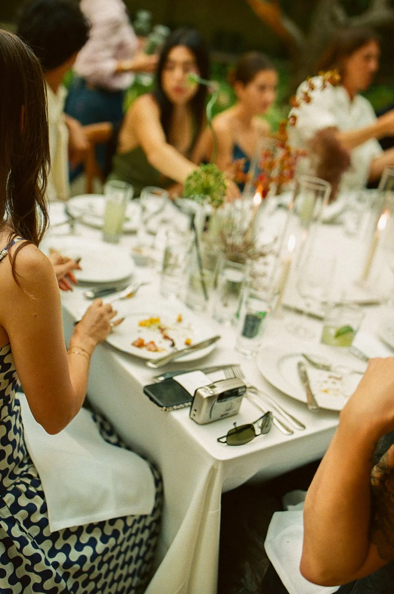 A candid dinner table moment showing guests seated at a long white table with floral centerpieces, glassware, and candles, capturing Intimate Wedding Ideas for a garden-style reception.