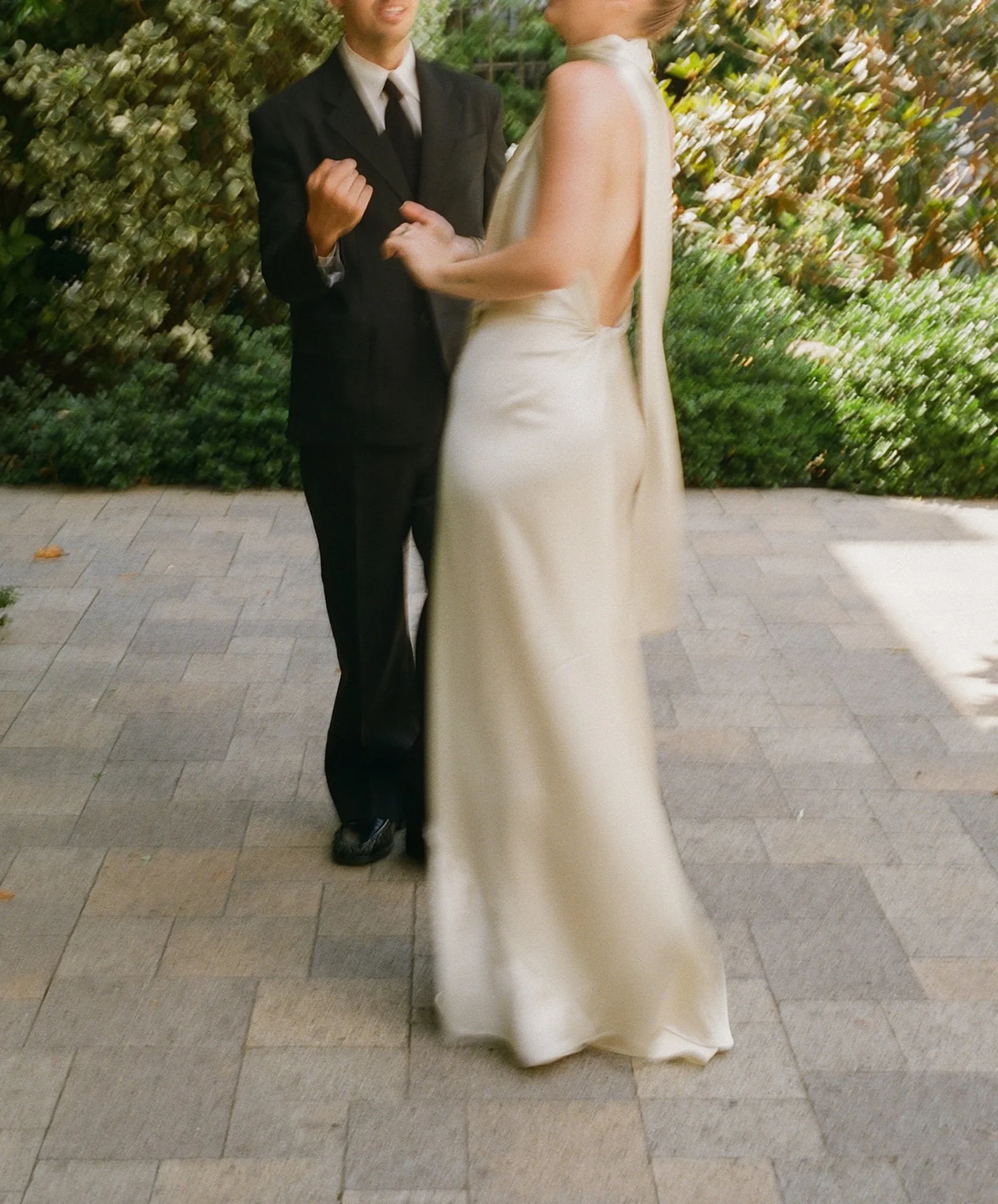 A couple having their first look at an outdoor wedding reception at Redbird, with the bride in a sleek satin halter gown and the groom in a black suit, surrounded by greenery and soft natural light.