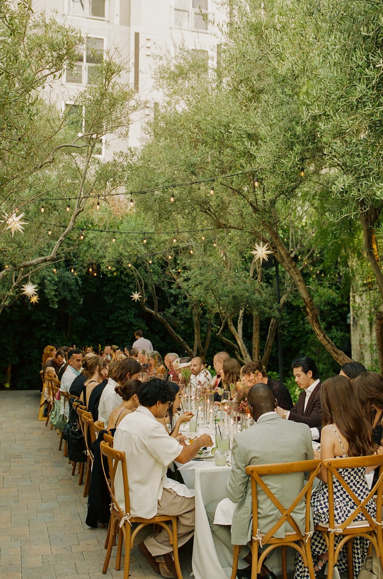 A long banquet table filled with guests dining outdoors under string lights, creating a romantic atmosphere for Intimate Wedding Ideas and alfresco wedding dinners.