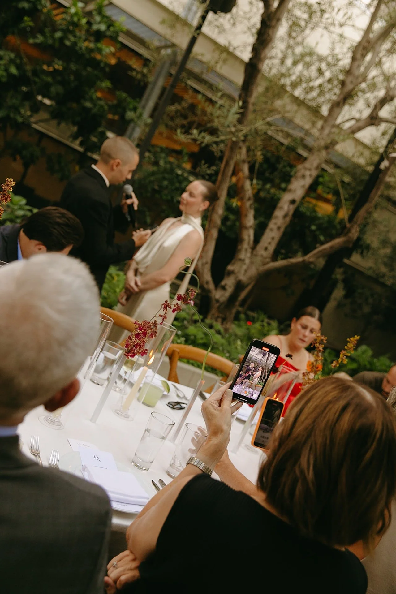 A tilted, documentary-style shot of guests recording the couple’s vows on their phones, capturing Intimate Wedding Ideas with a candid, editorial perspective.