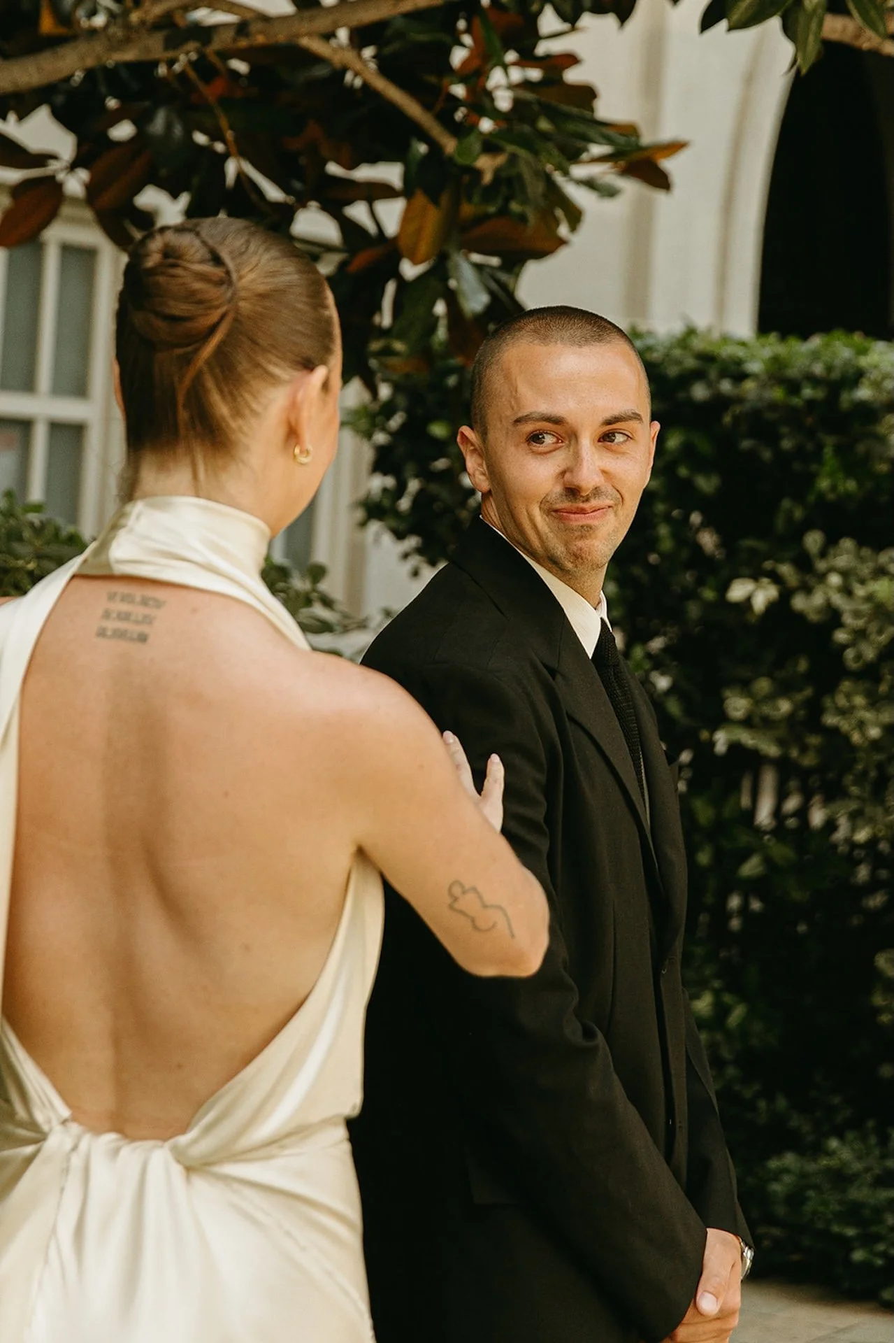 The groom turning to smile at the bride during their first look, with the bride touching his shoulder in a lush garden setting.