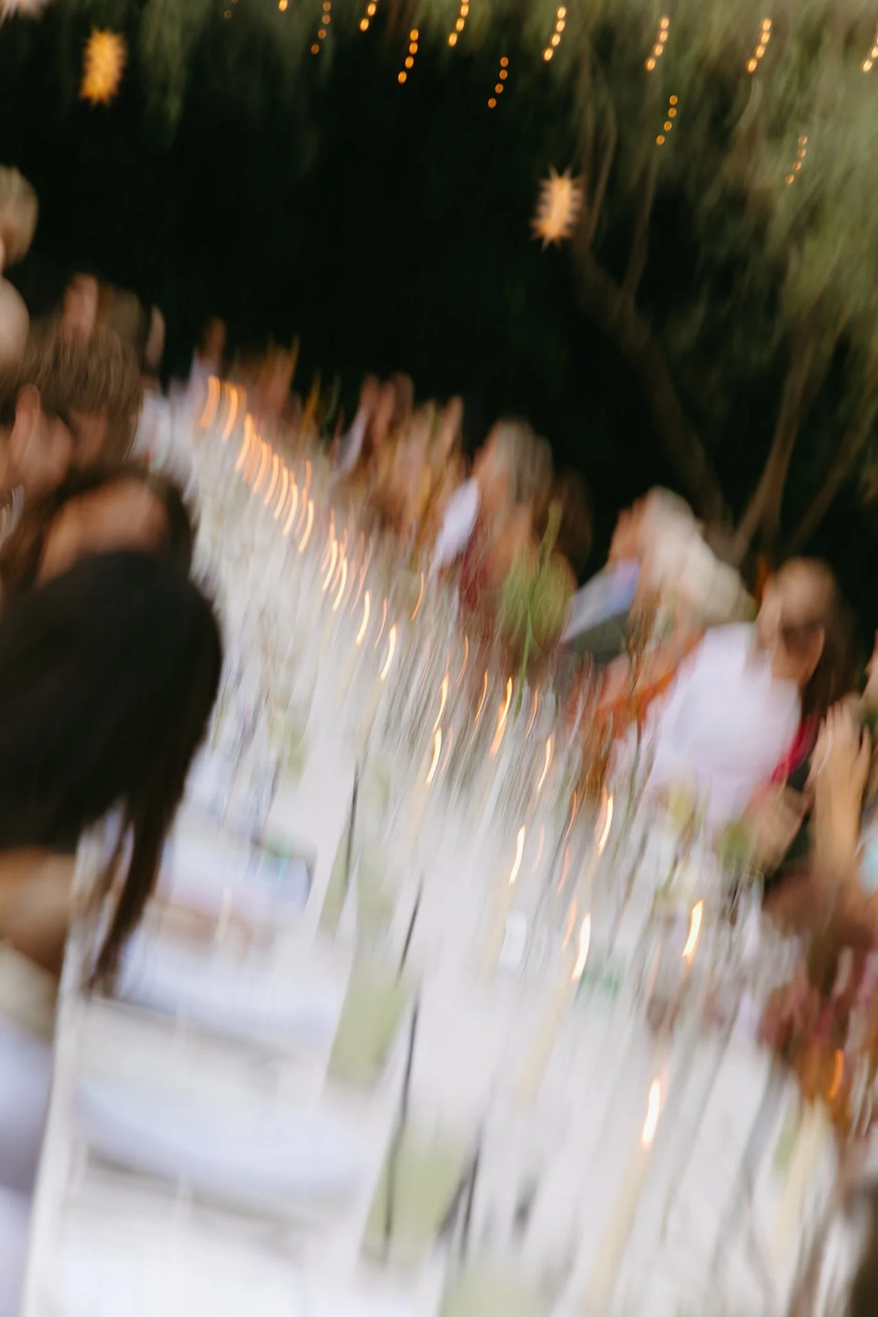 A blurred motion shot of guests seated at a long dinner table with candles and string lights, capturing Intimate Wedding Ideas with an artistic, documentary aesthetic.