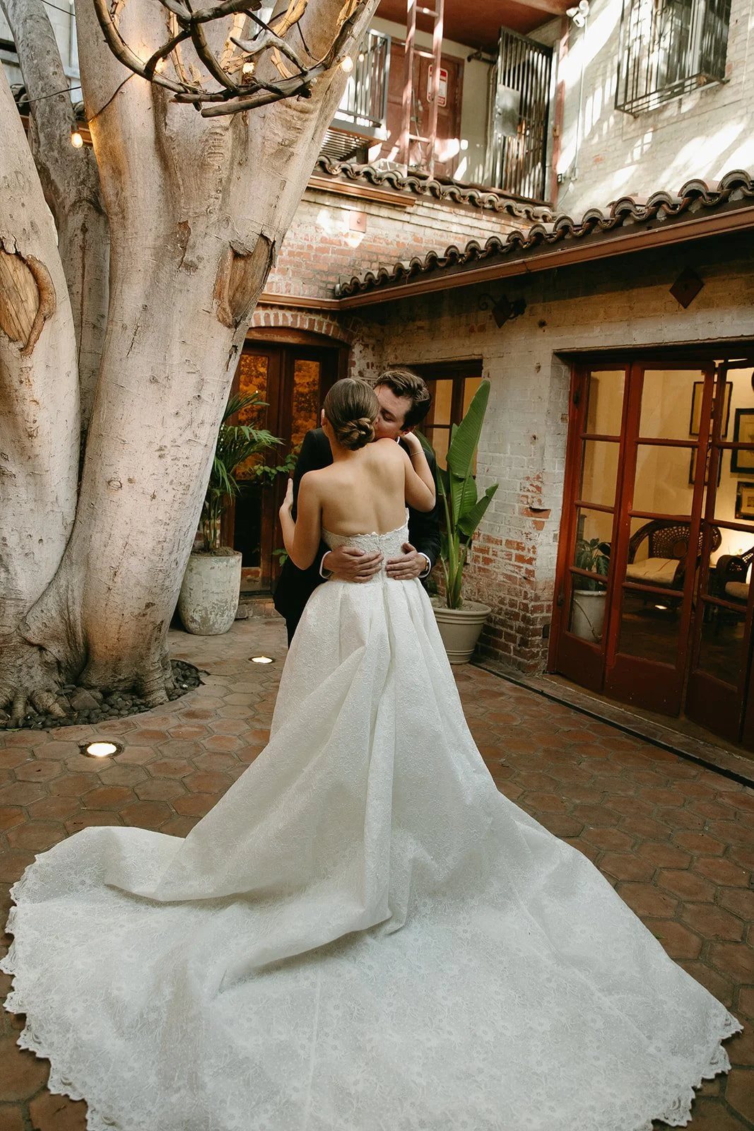 A wide shot of a bride in a textured ballgown and a groom in a black tuxedo embracing in the courtyard of one of the historic DTLA wedding venues.