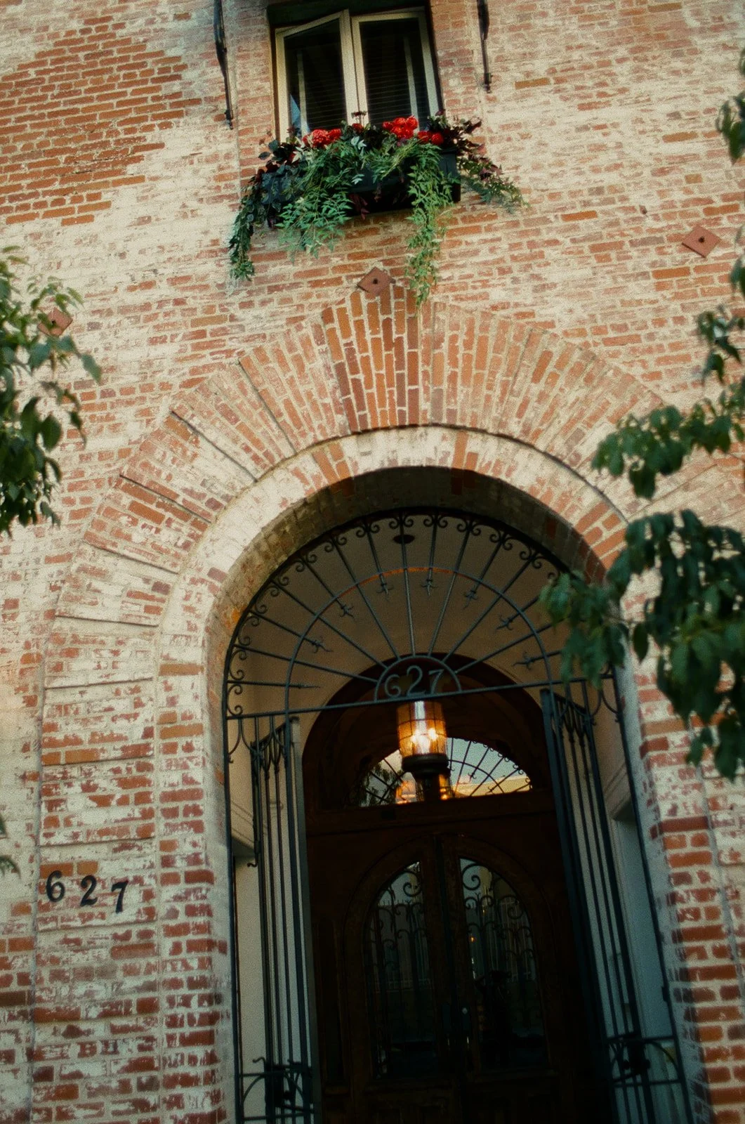The exterior brick facade of Carondelet House, showing a decorative arched entryway with a wrought-iron gate and a window box filled with red flowers.