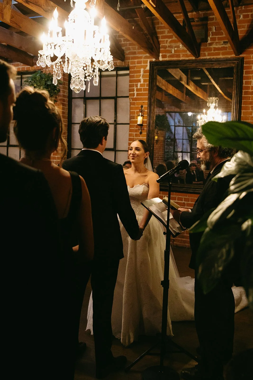 The bride and groom standing in a dimly lit room as the officiant reads their vows.
