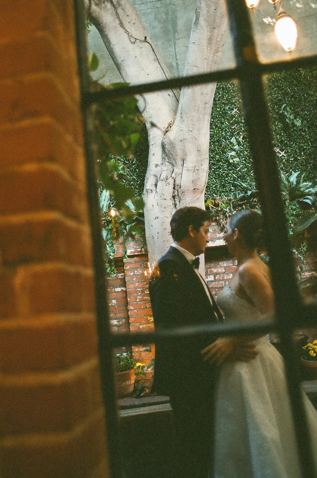 The bride and groom sharing an intimate moment captured through a window pane.