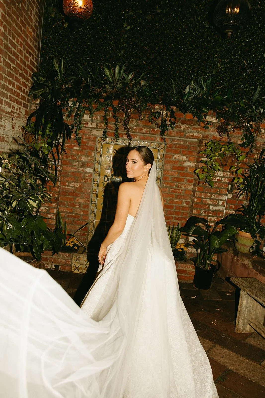 An editorial bridal photo of the bride with her back to the camera as her veil flows and she looks back at the camera.