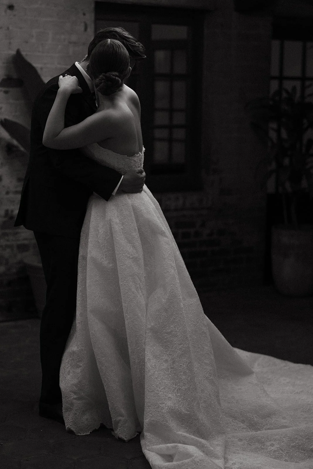 A black and white photo of the bride and groom standing in the courtyard at their  DTLA wedding venue hugging onto each other during their bride and groom portraits.