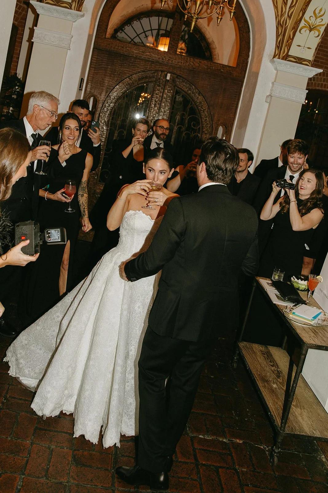 A bride and groom dancing and drinking with their wedding guests on the dance floor during their wedding reception.