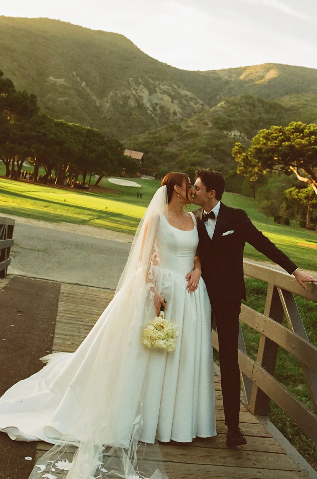Newlyweds kissing on a wooden bridge with scenic mountain views and golden hour light in Laguna Beach.